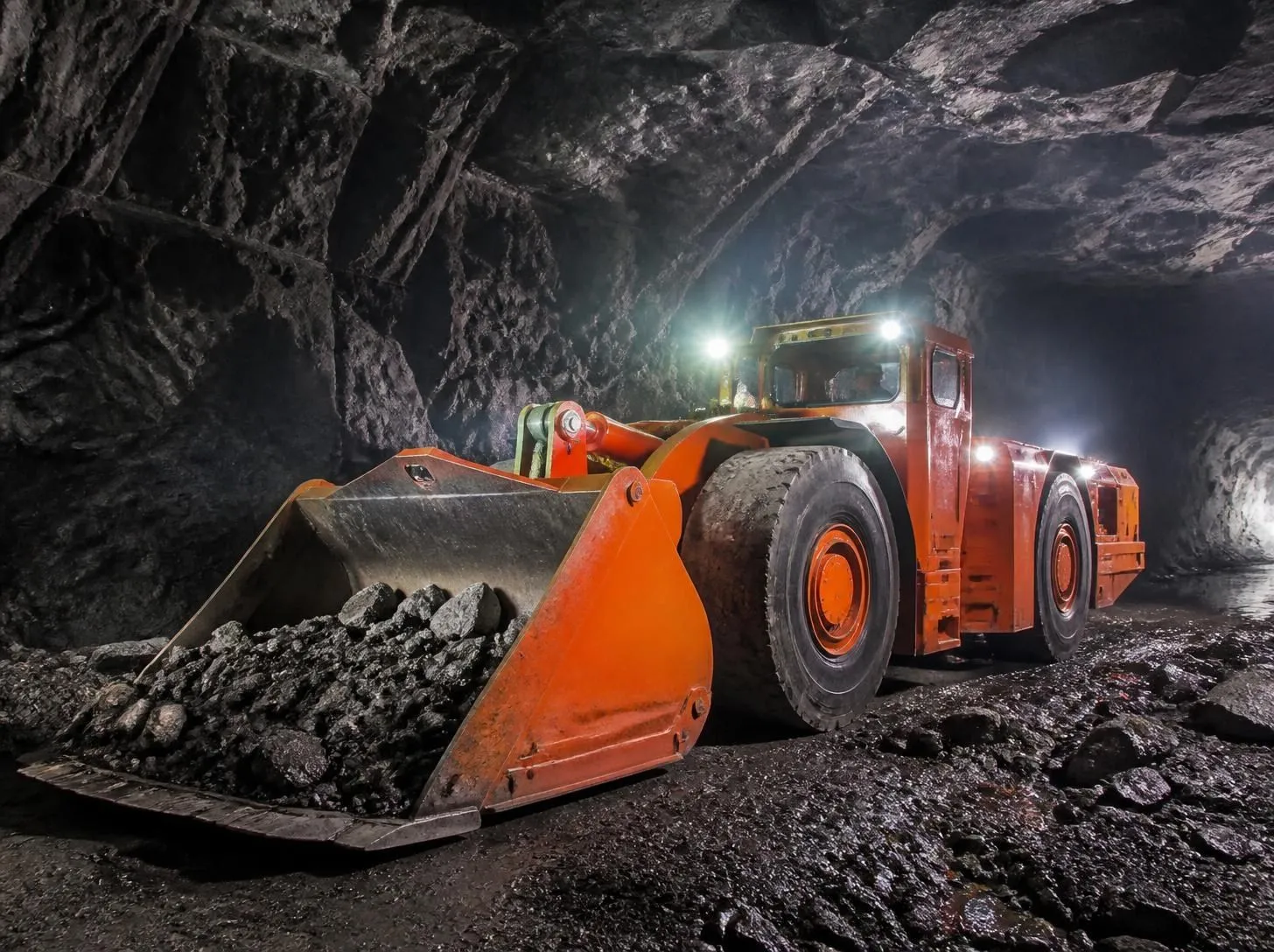 Underground mining loader (LHD) hauling rock inside a dark underground tunnel